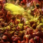 Vibrant crowd celebrating Holi 2026 in India, throwing colorful gulal powder in the air during the traditional festival of colors.